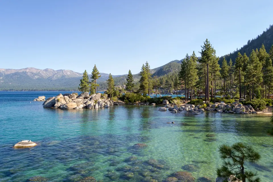 Clear turquoise water and granite boulders in a pine-lined cove on Lake Tahoe