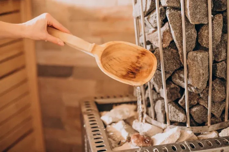 Water poured from a wooden ladle onto hot stones in a wood-lined sauna